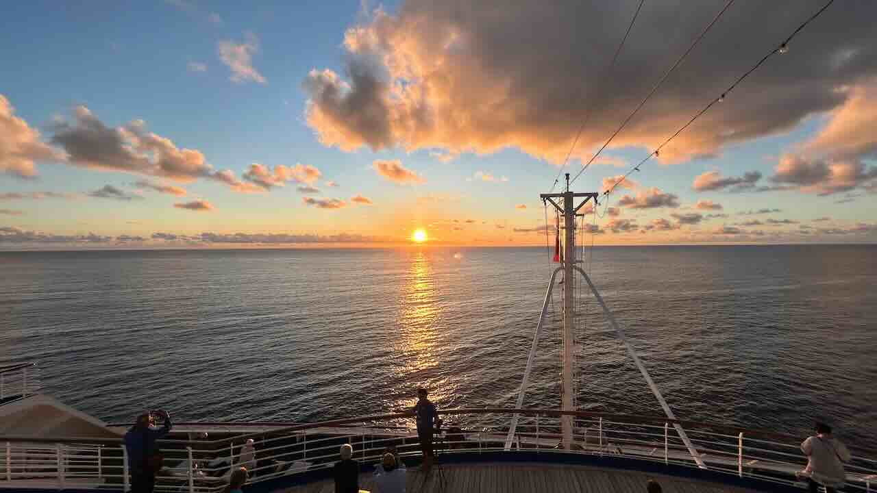 ピースボートがイースター島を離れる夕暮れ時、デッキから見た美しいサンセット。黄金色の光が水平線に沈み、旅の終わりと新しい航海の始まりを感じさせる。