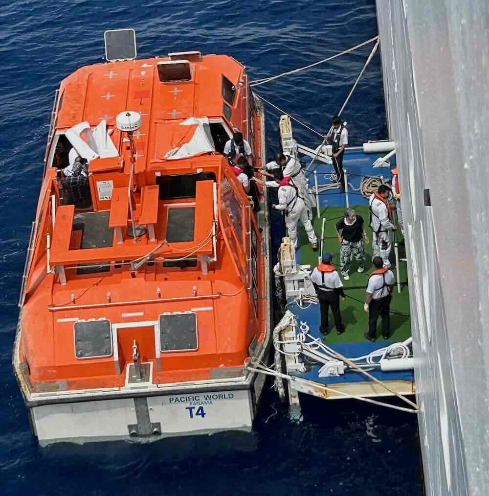 ピースボート「パシフィック・ワールド号」からイースター島へ向かうため、乗客がオレンジ色のテンダーボートに乗り込む様子。上陸前の緊張感と青い海のコントラストが印象的。