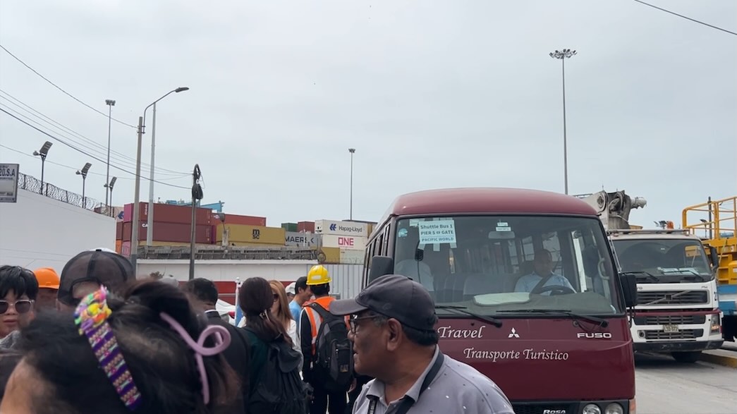 カヤオ港の港外バス降り場で、乗客をタクシーに割り振っている現地係員のおじさん。周囲には下船した乗客と、送迎バスやトラックが並び、混雑する様子が映っている。