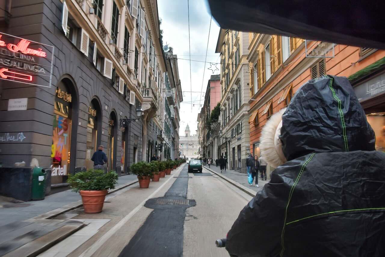 ジェノバ旧市街の通りを人力車で進む様子。ガイドの後ろ姿から街の日常が伝わる風景
