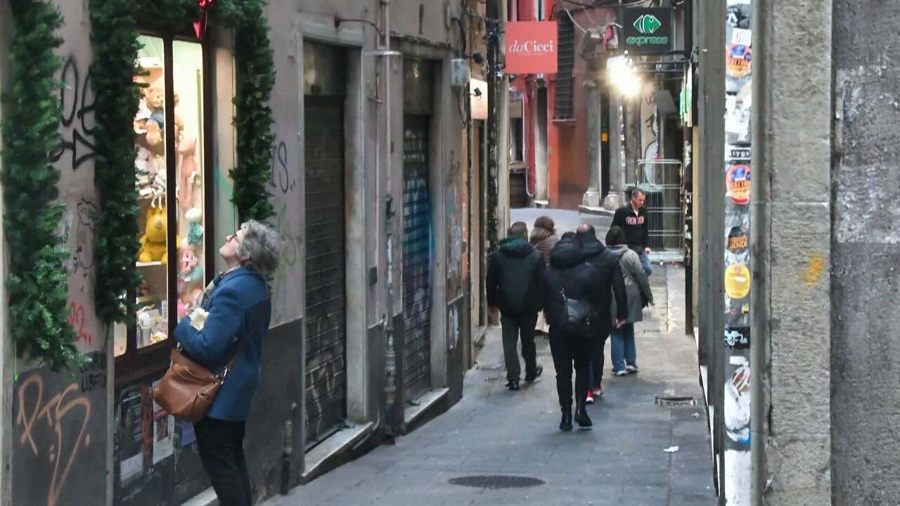 ジェノバ旧市街の路地でショーウインドウを見上げる地元の高齢女性。生活感のある街並み