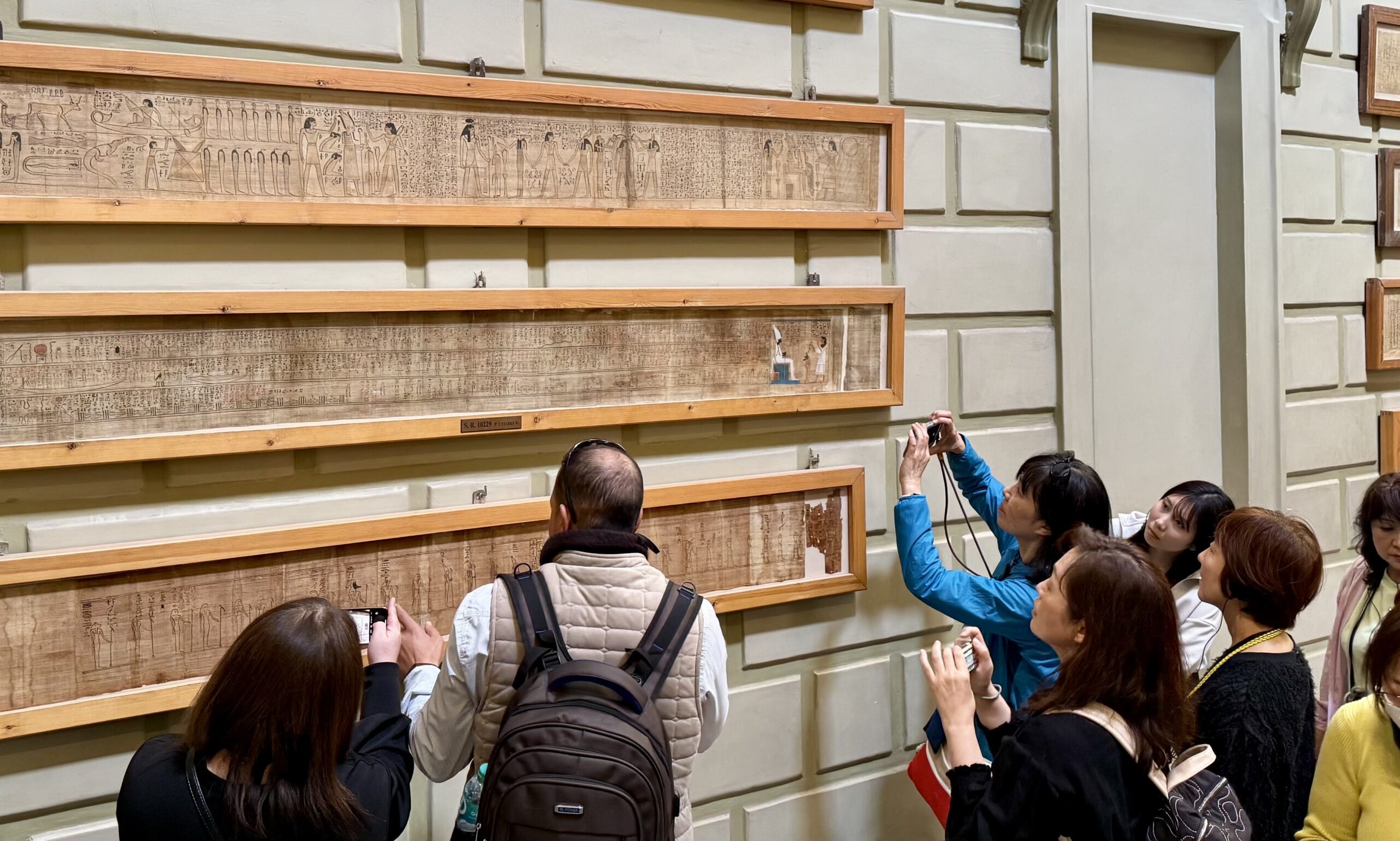 壁に飾られた古代パピルスと、それを見る観光客たち