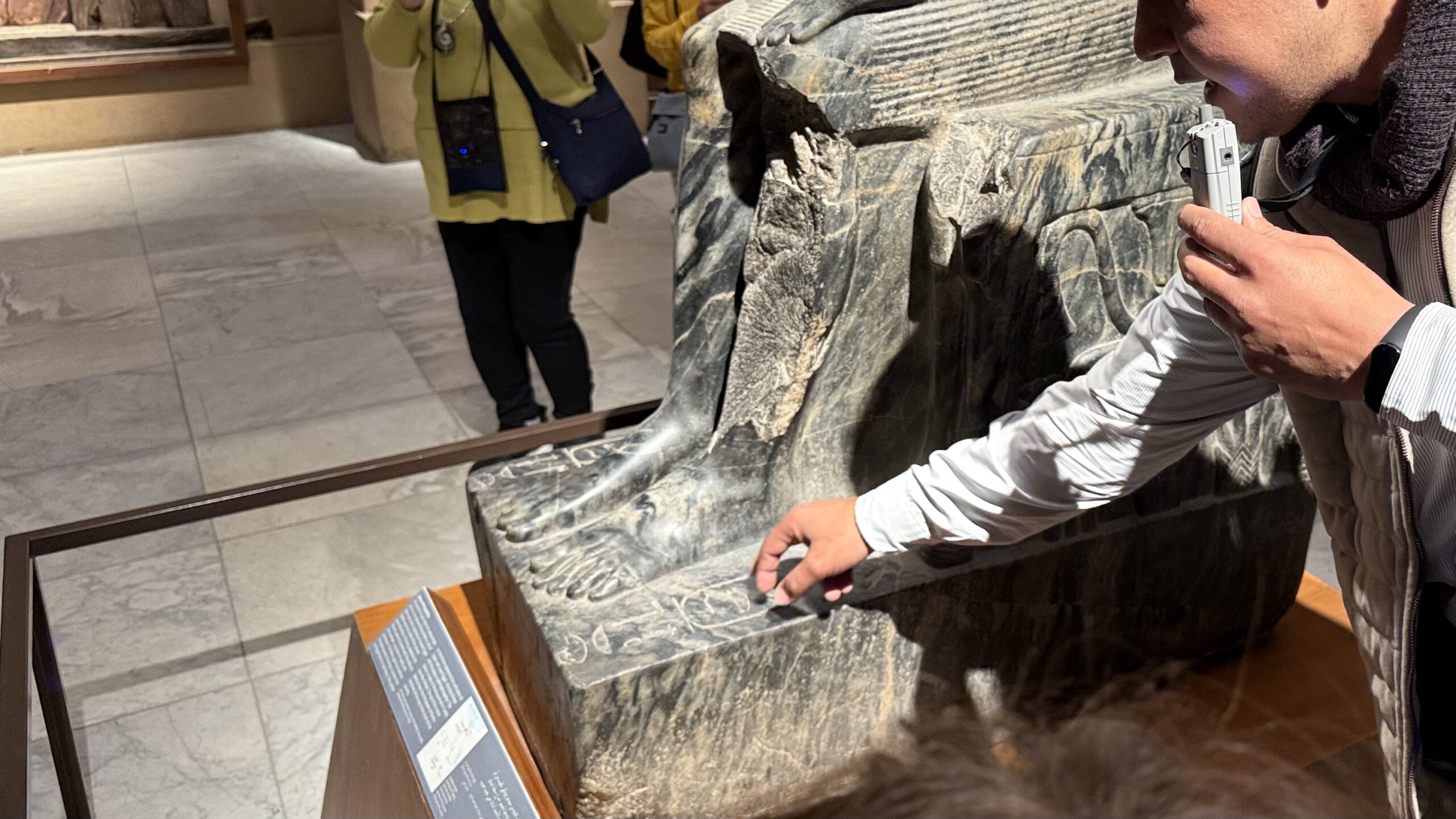 石像の足元を指さすガイドと観光客