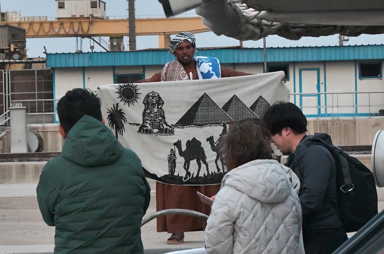 エジプトでスカーフを広げて見せる商人とツアー客