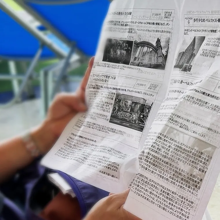 パシフィック・ワールドのデッキでイベント案内が載った船内新聞を読む手元