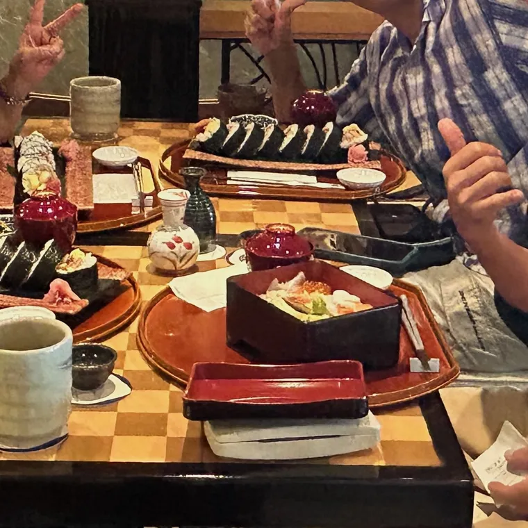 巻き寿司や小鉢を並べた食卓を囲み、手でピースや親指を立てる人たち