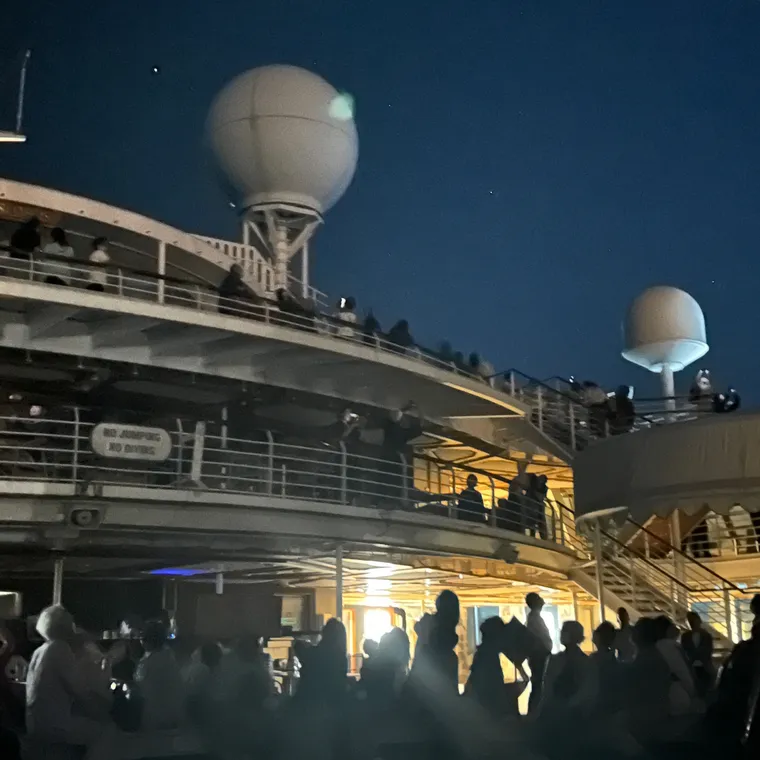 夜のデッキに集まる大勢の乗客と船のレーダードーム