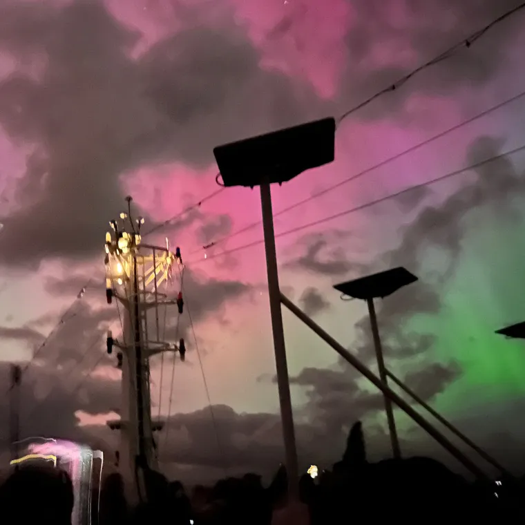 船のマストと厚い雲の間に見えるピンクと緑のオーロラ