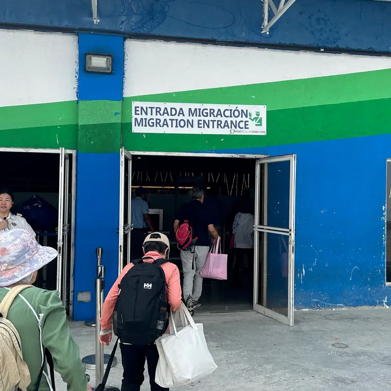 青と緑の建物にある入国口を、荷物を持った人々が通る