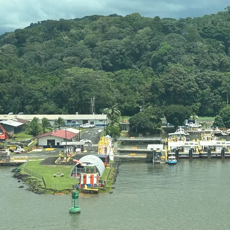 パナマ運河の緑の斜面と、水路沿いの建物や小型の船
