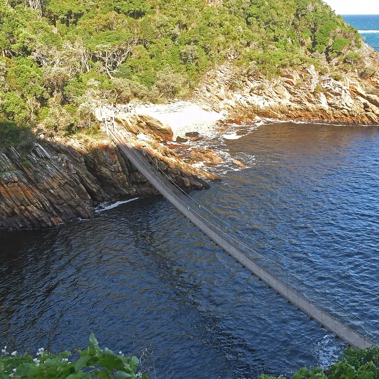 ツィツィカマの水辺に架かる吊り橋と緑の斜面