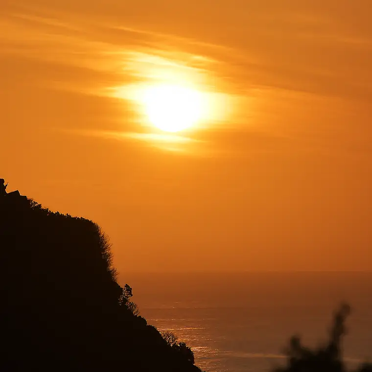 崖の向こうに沈みかけた太陽とオレンジ色の海と空