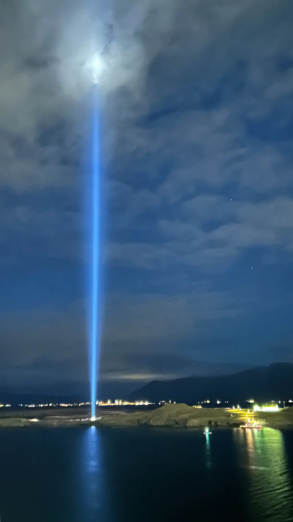 夜の海に向かって伸びるイマジンピースタワーの光の柱