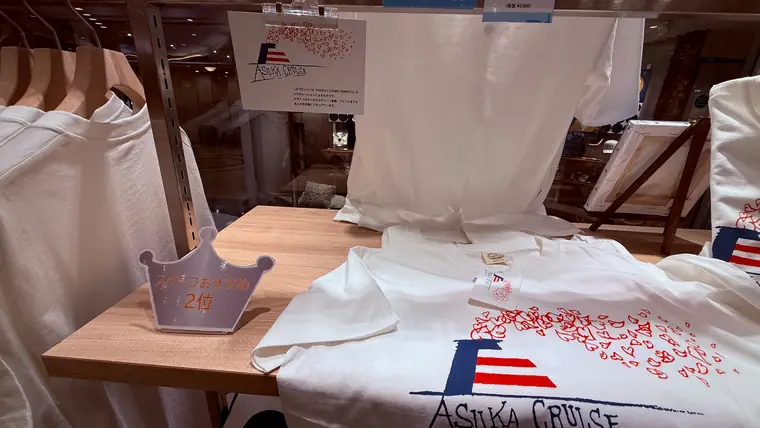 船内ショップの台に並ぶ飛鳥Ⅱの白いオリジナルTシャツ