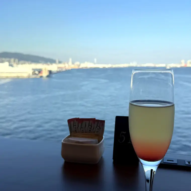 窓の外に神戸港を望むパームコートのテーブルとウェルカムドリンク